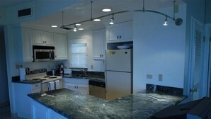 A modern kitchen with white cabinets, a granite countertop, stainless steel appliances, and recessed lighting.