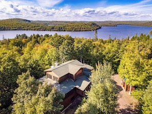 Una cabaña rodeada de un bosque frondoso con un lago al fondo.