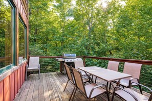 A wooden deck with a grill and seating area overlooking a forested area.
