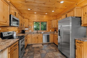 A modern kitchen with wooden cabinets, stainless steel appliances, granite countertops, and a large window.