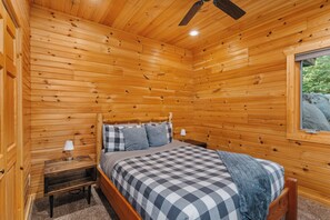 A wooden cabin bedroom with a bed, nightstand, lamp, and a window. - Northern Comfort Overlooking Caribou Lake- Spacious and Secluded (Lutsen)