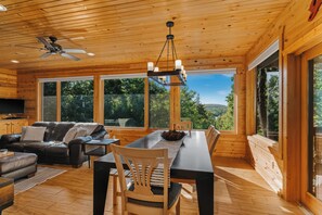 A spacious room with a wooden ceiling, large windows, a dining table, and a leather sofa. - Northern Comfort Overlooking Caribou Lake- Spacious and Secluded (Lutsen)