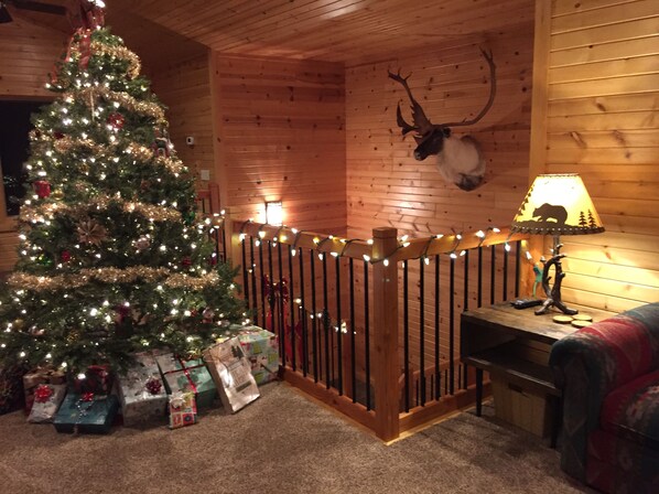 A cozy cabin interior with a decorated Christmas tree, presents, a deer head on the wall, and a lamp on a table. - Northern Comfort Overlooking Caribou Lake- Spacious and Secluded (Lutsen)