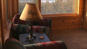 A cozy cabin interior with a large window offering a view of a forest and lake.