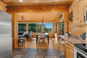 A wooden cabin interior with a dining area, kitchen, and a large window offering a view of the outdoors. - Northern Comfort Overlooking Caribou Lake- Spacious and Secluded (Lutsen)
