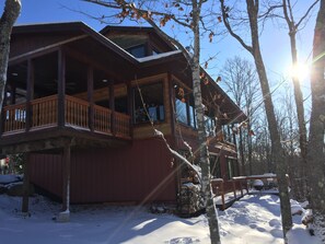 A wooden cabin with a balcony and a covered deck, surrounded by snow and trees. - Northern Comfort Overlooking Caribou Lake- Spacious and Secluded (Lutsen)