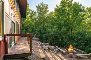 A wooden deck with a fire pit, surrounded by rocks and trees. - Northern Comfort Overlooking Caribou Lake- Spacious and Secluded (Lutsen)