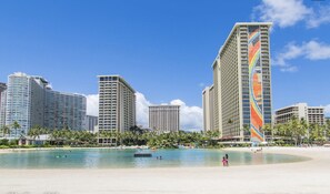 Un hôtel situé en bord de mer, composé de plusieurs immeubles de grande hauteur, avec une plage de sable fin et un ciel bleu dégagé.