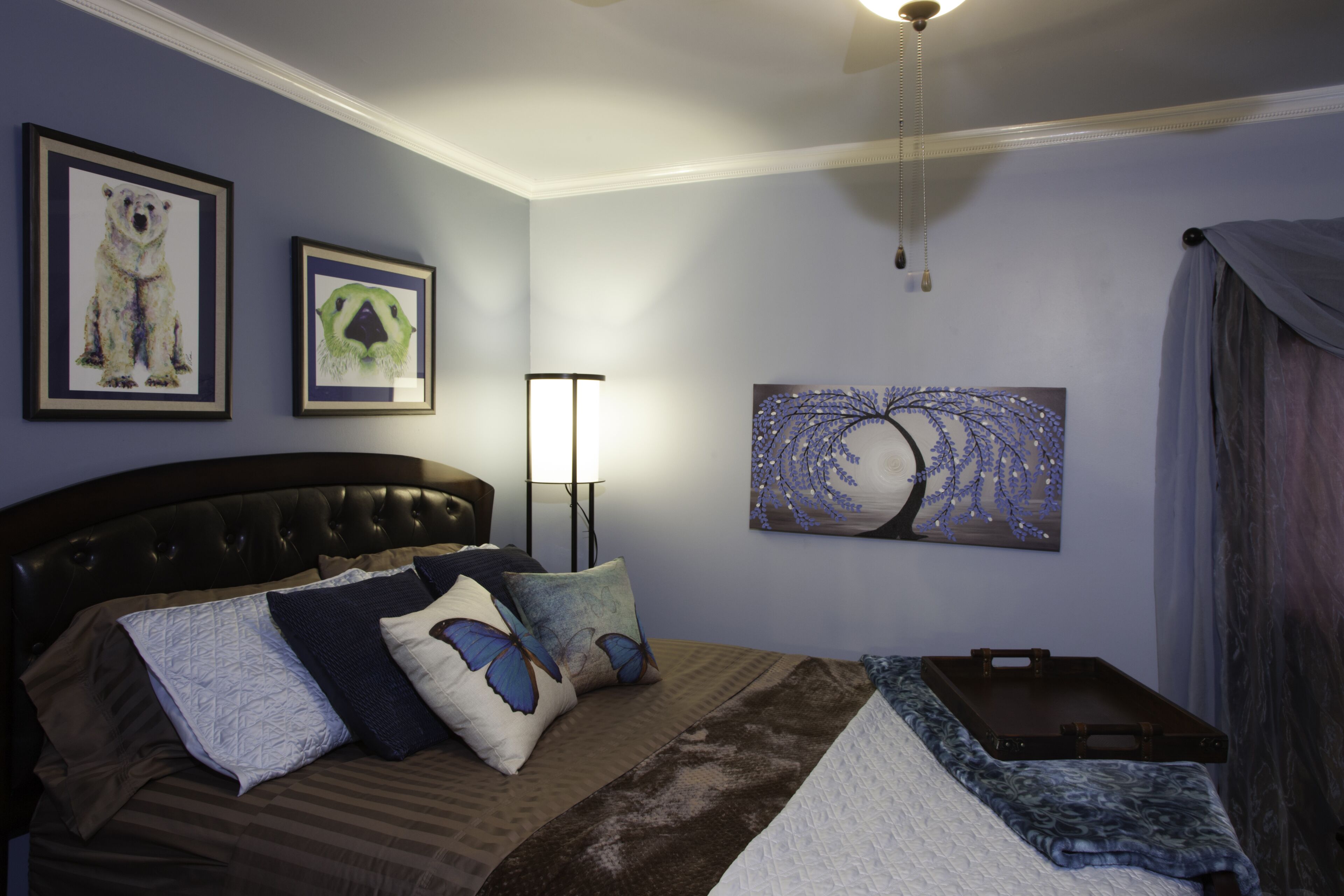 A bedroom with a bed, pillows, a bedside table, a lamp, and artwork on the walls.