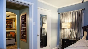 Un dormitorio con cama, mesita de noche, lámpara, cómoda y puerta que da a un baño.