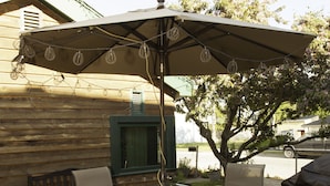 Un patio al aire libre con una mesa, sillas, un televisor con marco verde y un árbol.