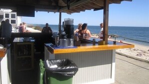 A beachside bar with a wooden counter, a trash bin, and a view of the ocean. - Great Location, Beach 4 minutes walk, Large Patio and Parking for one vehicle. (Dennis)