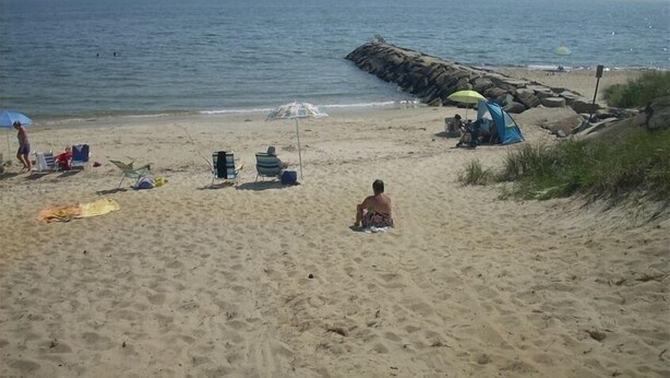 A sandy beach with a rocky breakwater, a tent, and a few people. - Great Location, Beach 4 minutes walk, Large Patio and Parking for one vehicle. (Dennis)