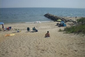 A sandy beach with a rocky breakwater, a tent, and a few people.