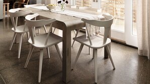 Un espace repas avec une longue table, des chaises blanches et une vue sur l’extérieur grâce à de grandes fenêtres.