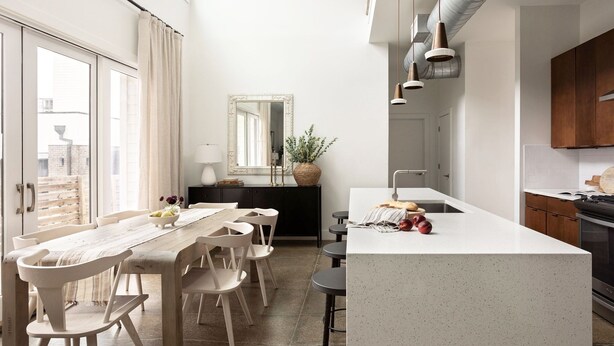 Une cuisine moderne dotée d’un îlot central, d’un coin repas avec une longue table et des chaises, et d’une grande fenêtre qui laisse entrer la lumière naturelle.