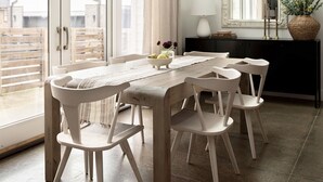 Un coin repas avec une table en bois et des chaises blanches, un grand miroir et un luminaire suspendu.