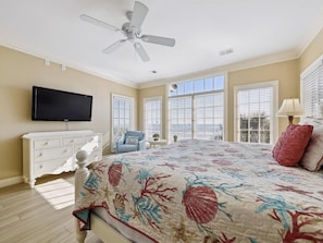 A bedroom with a bed, a ceiling fan, a TV, a dresser, and large windows. - Luxury Oceanfront Home in North Forest Beach! (Hilton Head Island)