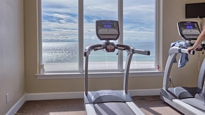Un gimnasio en casa con cinta de correr y elíptica, ventanas amplias con vista al océano.