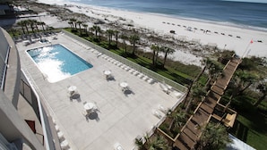 Un área de piscina en la azotea con sillones y mesas, con vistas a una playa y el océano.