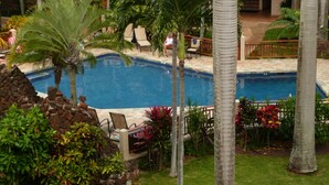 Un área de piscina con sillas de descanso, palmeras y un muro de piedra.