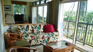 Sala de estar con sofá, sillas, una mesa de centro, televisor y balcón con vistas a zonas verdes.