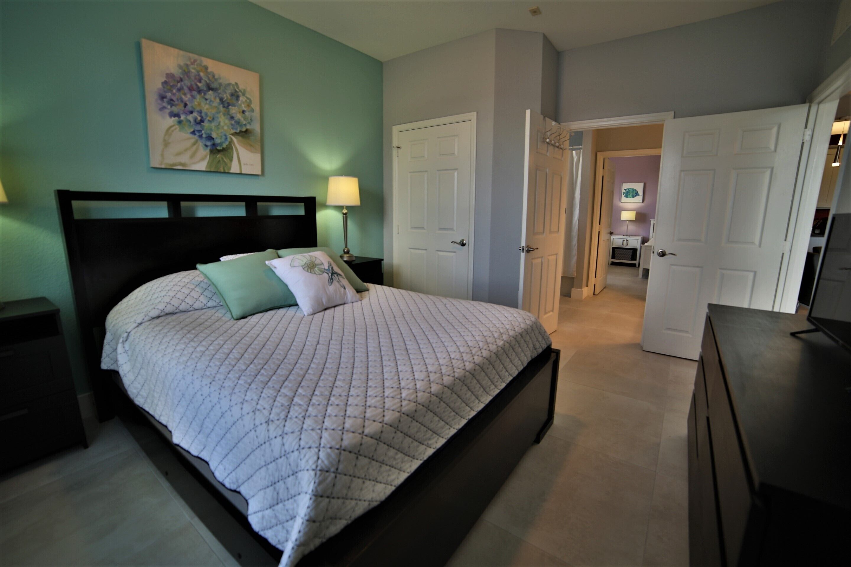 A bedroom with a bed, nightstands, a painting, and a door leading to a bathroom.