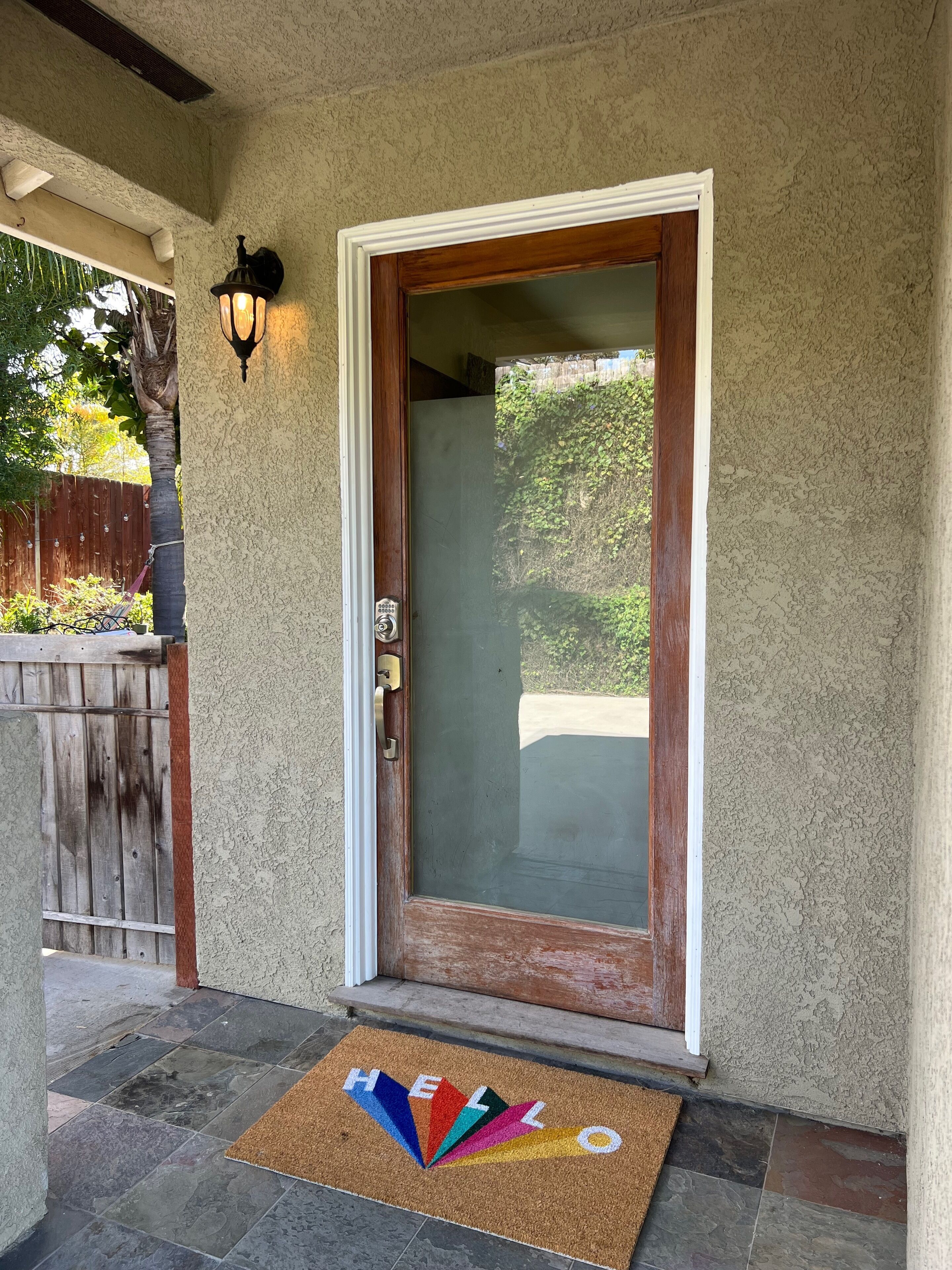 A front door with a frosted glass panel, a metal handle, and a doormat with "HELLO" spelled out in colorful letters.