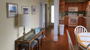 Una cocina con armarios de madera, un microondas, un horno y un refrigerador. Hay una mesa de comedor con sillas y un banco.