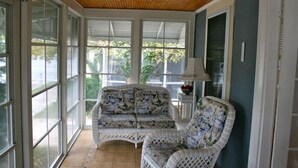 Un solárium con techo de madera, ventanas amplias, un sofá de mimbre y una mesita de noche con lámpara.