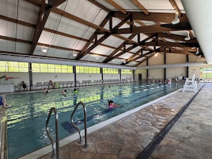 Une piscine intérieure dotée de plusieurs couloirs, de poutres en bois et d’un sol carrelé.