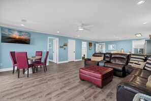 A spacious living area with a dining table, red chairs, a leather sofa, and a ceiling fan. - 4 bedrooms, Ocean Views, fireplace, entertainment room with large screen tv! (Edisto Beach)