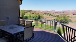 Un balcón con mesa y sillas, que ofrece vistas a un jardín ajardinado con árboles y montañas a lo lejos.