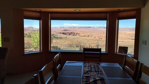 Un comedor con una mesa y sillas, ventanas amplias con vista a un paisaje desértico.