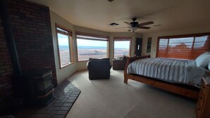 Un dormitorio con chimenea, una cama, un ventilador de techo y ventanas amplias que ofrecen vistas del paisaje.