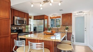 A modern kitchen with wooden cabinets, stainless steel appliances, a granite countertop, and a central island with bar stools. - Waterfront, saltwater lagoon, 2 pools, ocean access, marina, tennis, pickleball (Key Largo)