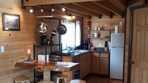 Un interior de madera con área de cocina, taburetes de bar y una mesa de comedor.