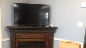 Ein Zimmer mit dunklem Holzofen, einem darüber montierten Fernseher und einer kleinen Staffelei an der Wand.