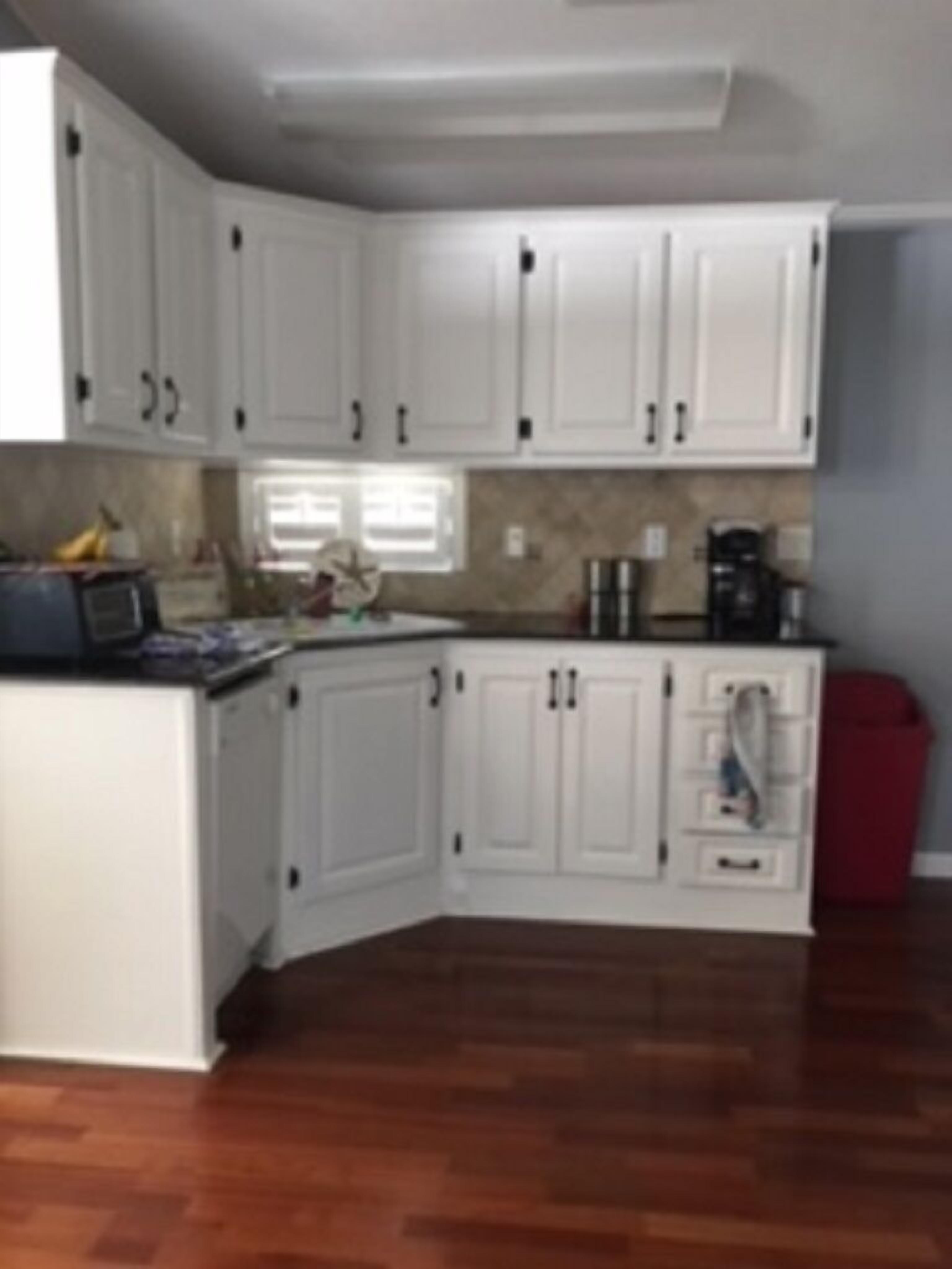 A kitchen with white cabinetry, a wooden countertop, and a red trash bin.