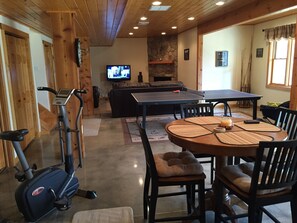 A living room with a stone fireplace, a television, a ping pong table, and exercise equipment.