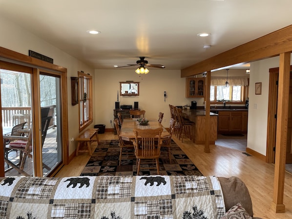 A spacious dining area with a wooden table and chairs, a ceiling fan, and a view of the deck through glass doors.