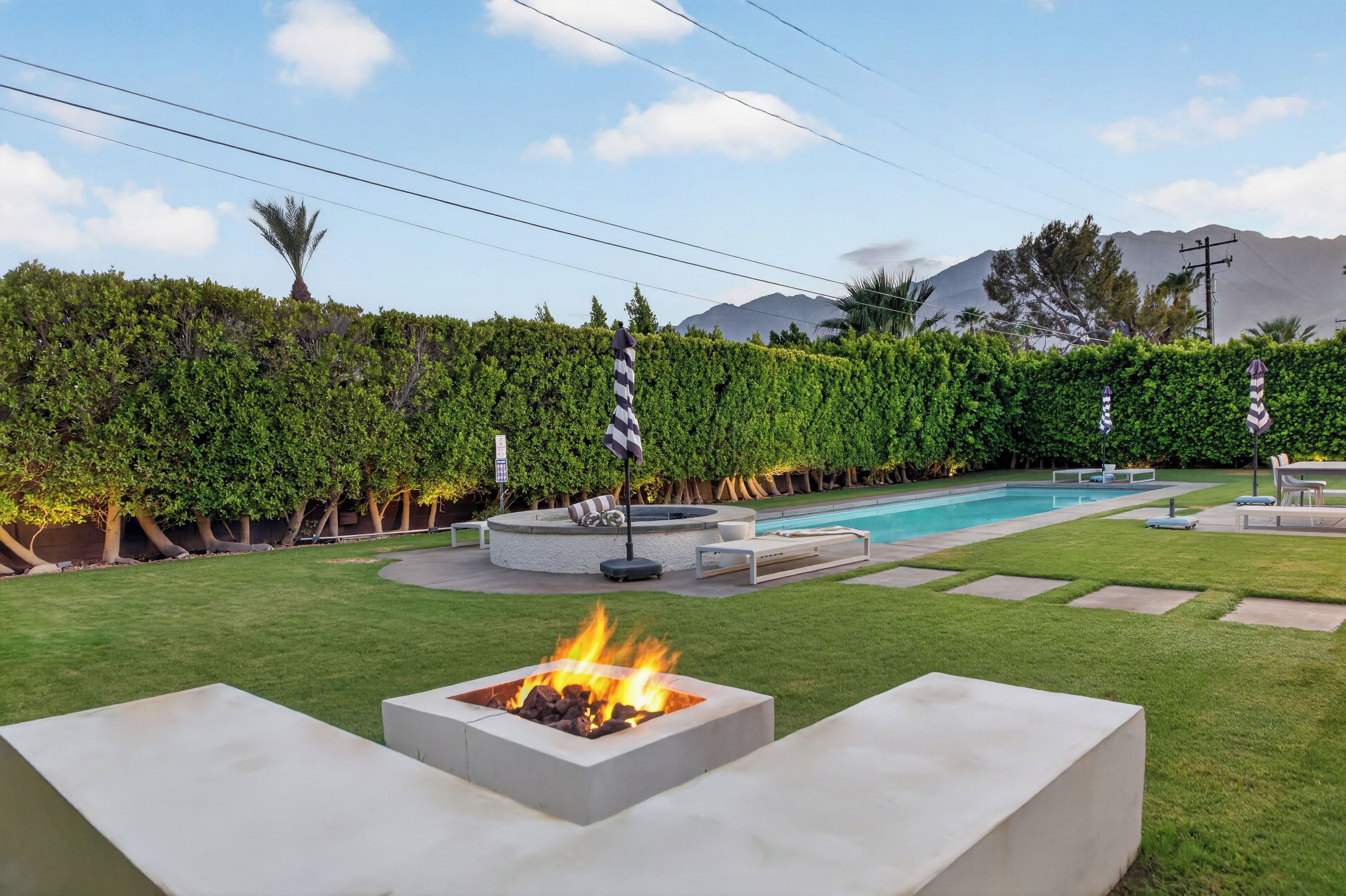 A backyard with a swimming pool, a fire pit, and a well-maintained lawn.