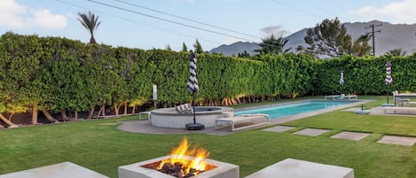 A backyard with a swimming pool, a fire pit, and a well-maintained lawn.