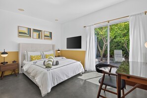 Ein Hotelzimmer mit einem Bett, einem Schreibtisch, einem Sessel, einem Fernseher und einem Fenster mit Vorhängen.