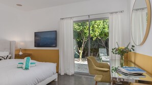 A hotel room with a bed, a chair, a desk with a mirror, and a view of a garden through a sliding door. - PS Chill: Meticulous Mid-Century Features Modern Comfort and Views! (Palm Springs)