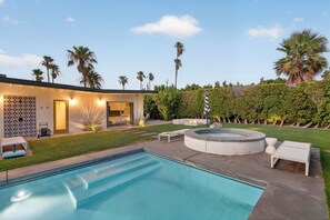 A modern outdoor pool area with a hot tub, lounge chairs, and a well-maintained lawn.