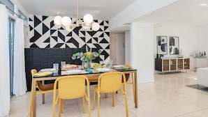 A dining area with a black and white geometric wall, yellow chairs, and a chandelier. - PS Chill: Meticulous Mid-Century Features Modern Comfort and Views! (Palm Springs)