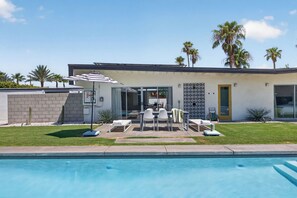 Une maison moderne dotée d’une piscine, de mobilier de jardin et de palmiers.