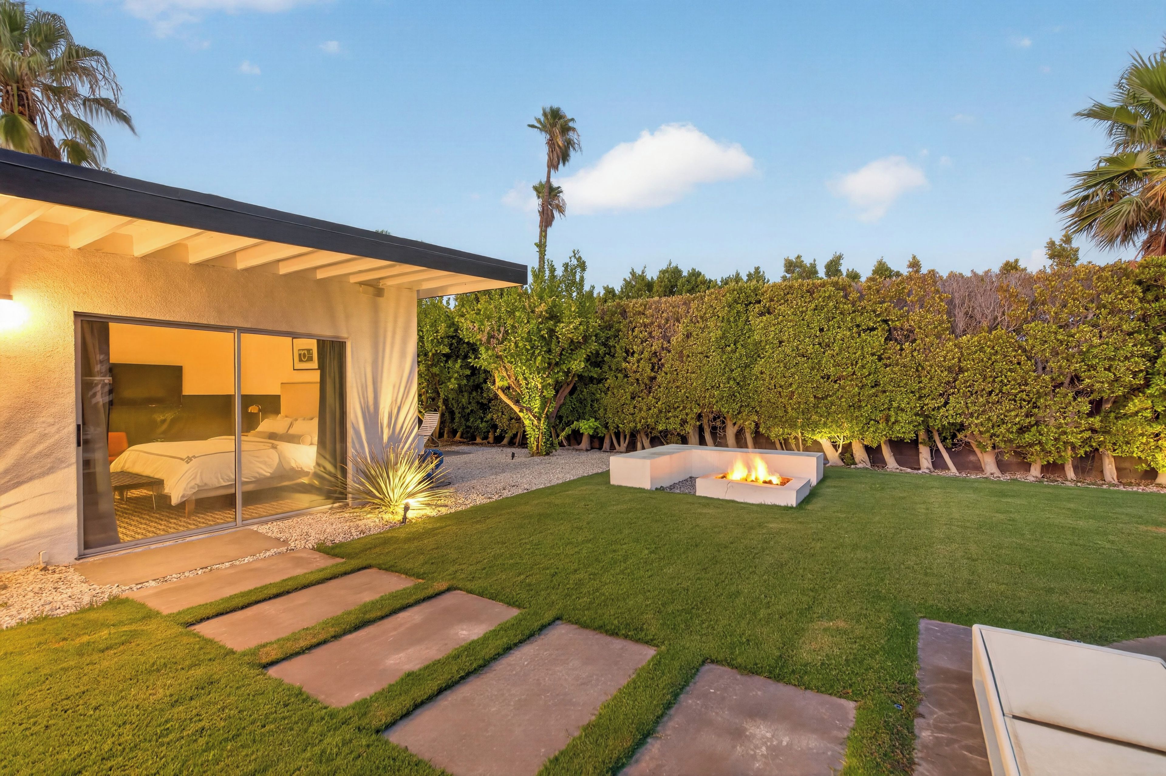 A modern outdoor space with a glass-enclosed bedroom, a fire pit, and a well-maintained lawn.