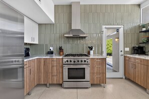 A modern kitchen with a built-in oven, a stainless steel range, and wooden cabinets. - PS Chill: Meticulous Mid-Century Features Modern Comfort and Views! (Palm Springs)
